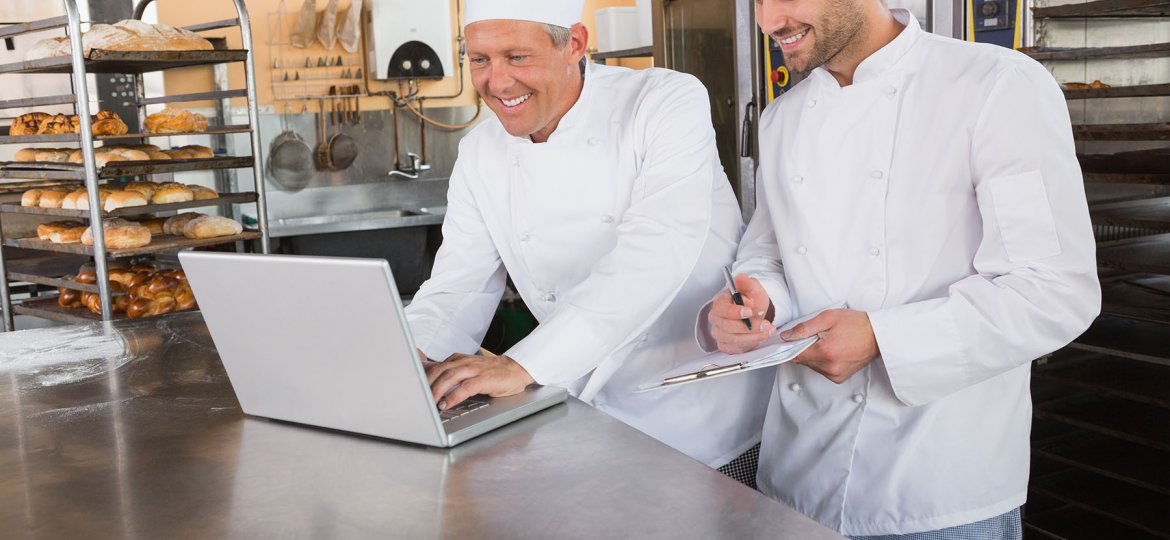 Smiling bakers working together on laptop in the kitchen of the bakery